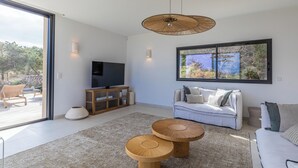 Ein modernes Wohnzimmer mit großem Fenster, einem Flachbildfernseher, einem weißen Sofa und zwei runden Holztischen.