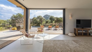 Ein modernes Wohnzimmer mit einem großen Schiebeglasfenster, das auf eine Terrasse im Freien führt.