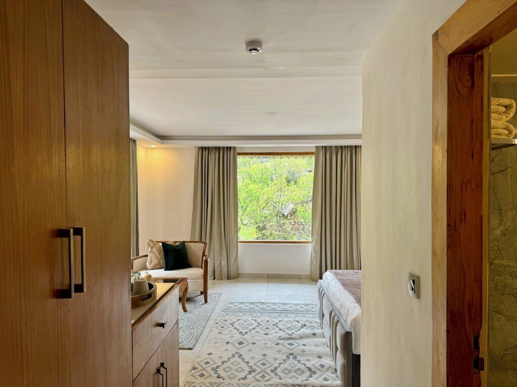 A bedroom with a bed, a chair, a wooden wardrobe, and a window with curtains.