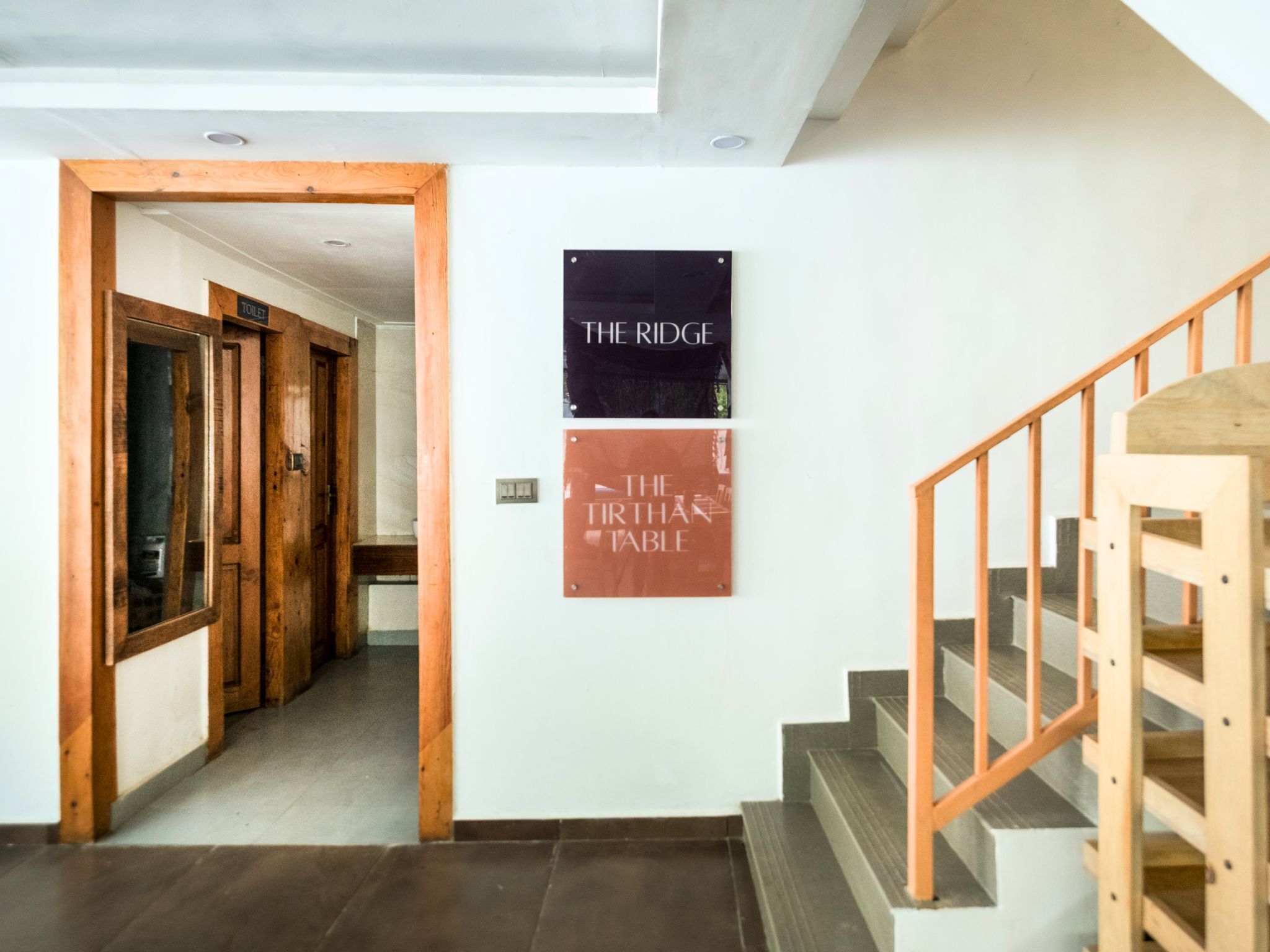 Un corridoio con porte in legno, una scala con ringhiere in legno e due cartelli appesi al muro con le scritte "THE RIDGE" e "THE THIRTHATABLE".