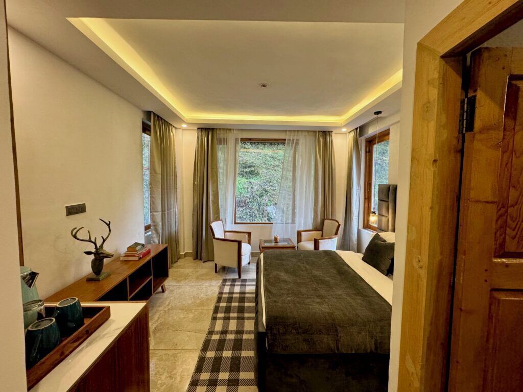 A modern hotel room with a bed, seating area, and a view of the outdoors.