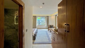 A hotel room with a bed, a wooden wardrobe, a bathroom with a towel rack, and a view of a house through a window. - Ausnya Tirthan (Banjar)