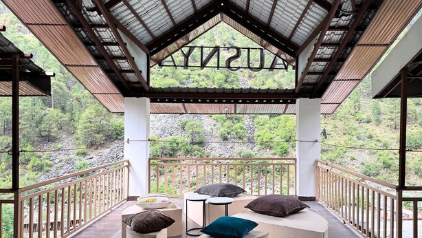 A covered outdoor seating area with a view of a forested landscape. - Ausnya Tirthan (Banjar)