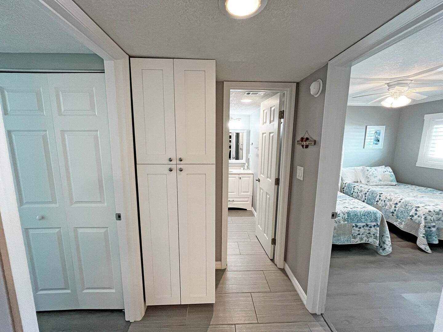 Ein schmaler Flur führt zu einem Schlafzimmer mit einem Bett und einem Fenster.