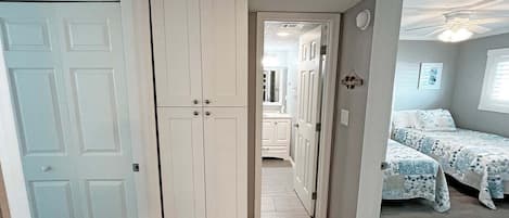 A narrow hallway leading to a bedroom with a bed and a window.