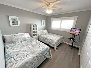 A bedroom with two beds, a ceiling fan, a window with blinds, and a television on a stand.
