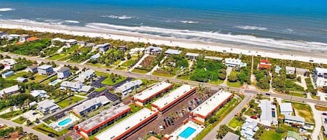 An aerial view of a coastal residential area with houses, a road, and a beach.