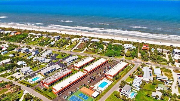 An aerial view of a coastal residential area with houses, a road, and a beach.