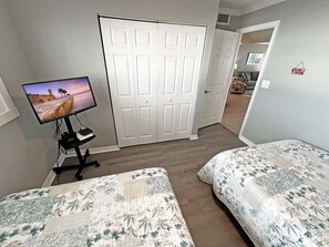 Un dormitorio con dos camas, un televisor sobre un soporte y un armario con puerta.