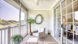 A balcony with wicker furniture, a potted plant, and a decorative wreath. - 133 River Crossing - Barefoot Resort Rentals (North Myrtle Beach)