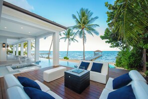An infinity pool with a wooden deck, white sofas with blue cushions, and palm trees.