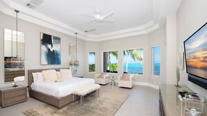 Een moderne slaapkamer met een groot bed, een plafondventilator, een televisie en uitzicht op de oceaan.