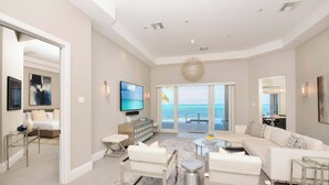 Een ruime woonkamer met een grote bank, een salontafel en een televisie. Er is een balkon met uitzicht op de oceaan.
