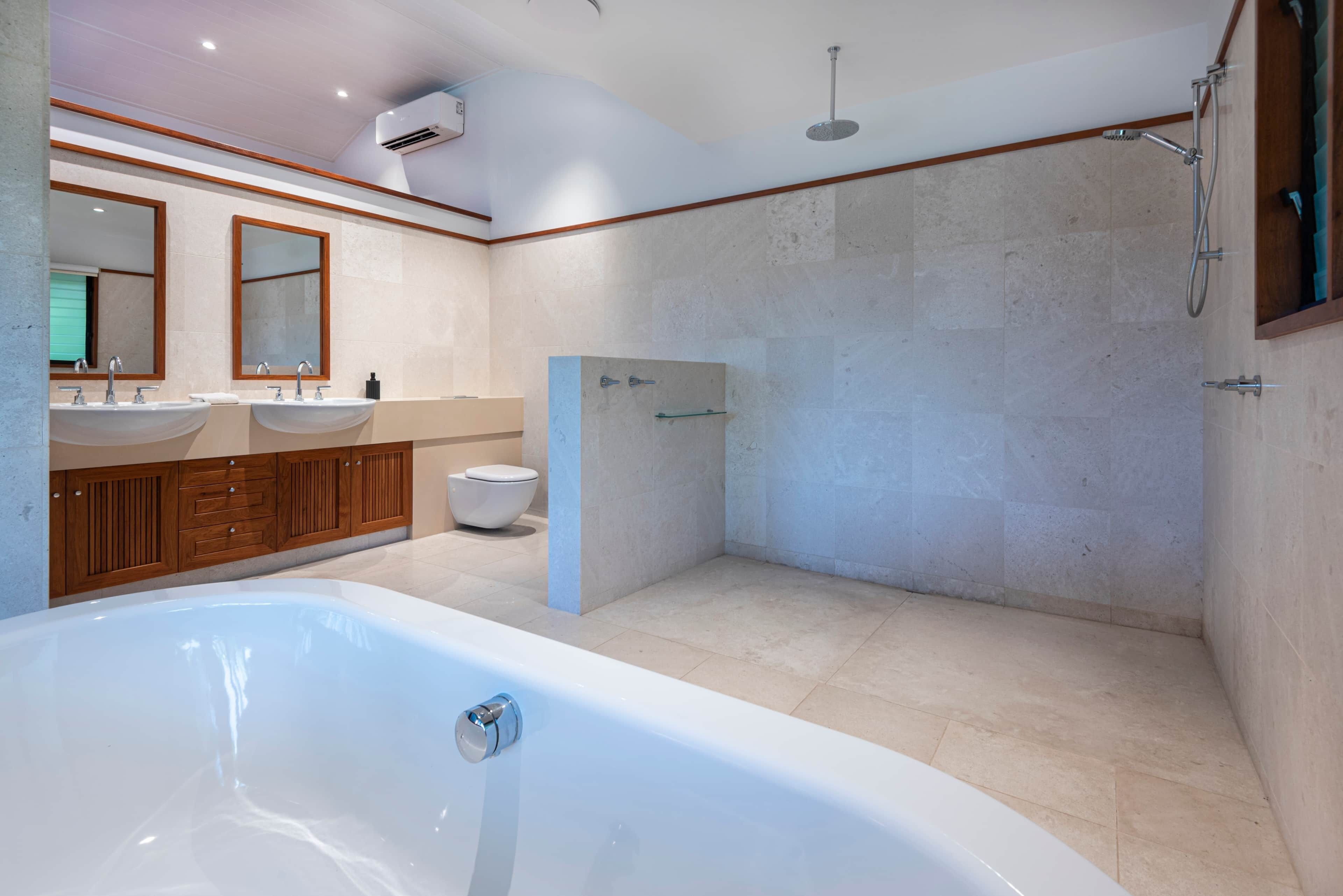 Een moderne badkamer met een bad, twee wasbakken, een douche en een toilet.