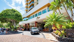 A hotel entrance with a car parked in front, palm trees, and a paved walkway. - Luana Waikiki Premium Studio- Gym & Pool (Honolulu)