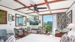 A hotel room with a large bed, two chairs, a small table, a ceiling fan, and a large window with a city view. - Luana Waikiki Premium Studio- Gym & Pool (Honolulu)