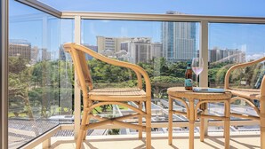 A balcony with wicker chairs and a table, overlooking a cityscape with high-rise buildings and greenery. - Luana Waikiki Premium Studio- Gym & Pool (Honolulu)