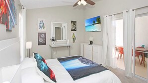 A bedroom with a bed, a ceiling fan, a TV, a desk, and a view of the beach through the window. - Amazing Game Room Salt Water Pool 10 Min to Disney (Kissimmee)