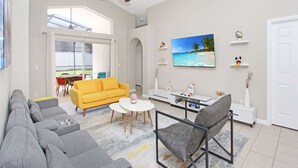 A modern living room with a sofa, armchairs, a coffee table, and a TV on the wall. - Amazing Game Room Salt Water Pool 10 Min to Disney (Kissimmee)