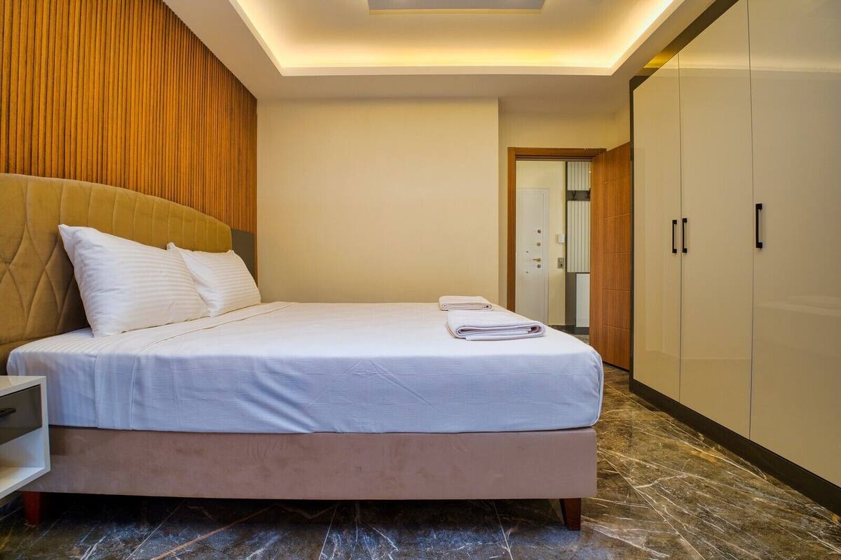 A neatly made bed with a headboard, a bedside table, and a wardrobe.
