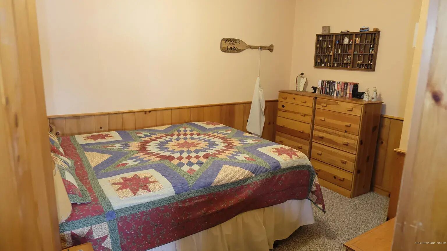 Ein Schlafzimmer mit einem hölzernen Bett, einer Steppdecke, einem Holzschrank und einem an der Wand befestigten Regal mit Büchern.
