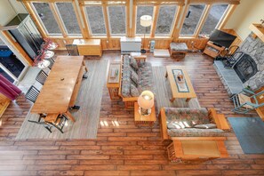 A spacious living area with a wooden floor, a sofa set, a dining table, and a fireplace. - Lake Front Cabin on Desirable Highland Lake (Bridgton)