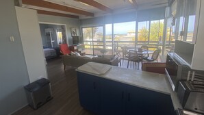 A modern kitchen with a central island, large windows offering a view of the outdoors, and a dining area with chairs and tables. - Straight to the Point - Sea views from balcony, dog friendly! (Pine Point)
