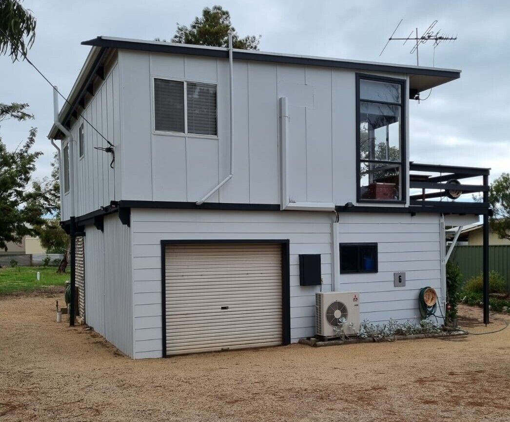 A two-story building with a garage, a large window on the upper floor, and an air conditioning unit outside.