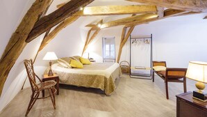 Une chambre avec un plafond en bois, un lit recouvert d’une couverture verte, une chaise en osier et une table de chevet avec une lampe.