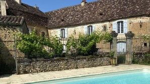 Une piscine avec un mur en pierre et un bâtiment doté d’un toit en tuiles et d’une façade en pierre.
