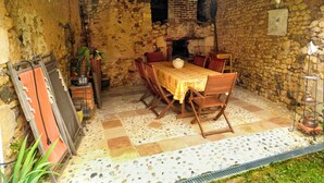 Une pièce rustique aux murs de pierre, avec une table et des chaises en bois, une cheminée et un sol carrelé.