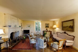 A living room with a fireplace, a sofa, chairs, a table, and a television. - La Chartreuse Périgord (Val de Louyre et Caudeau)