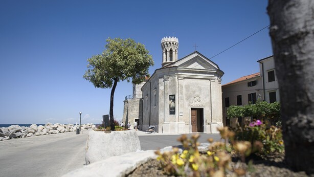 A church with a bell tower, a paved road, and a rocky shoreline. - Punta Apartment KA 2.2 (Piran)