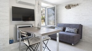 A modern living room with a grey sofa, a wooden dining table, and a flat-screen TV mounted on the wall. - Punta Apartment KA 2.2 (Piran)