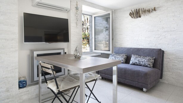 A modern living room with a grey sofa, a wooden dining table, and a flat-screen TV mounted on the wall. - Punta Apartment KA 2.2 (Piran)