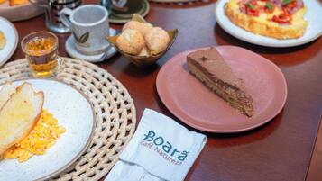 Uma mesa com itens de café da manhã, incluindo torradas, ovos mexidos, uma fatia de bolo de chocolate e um prato de pizza.