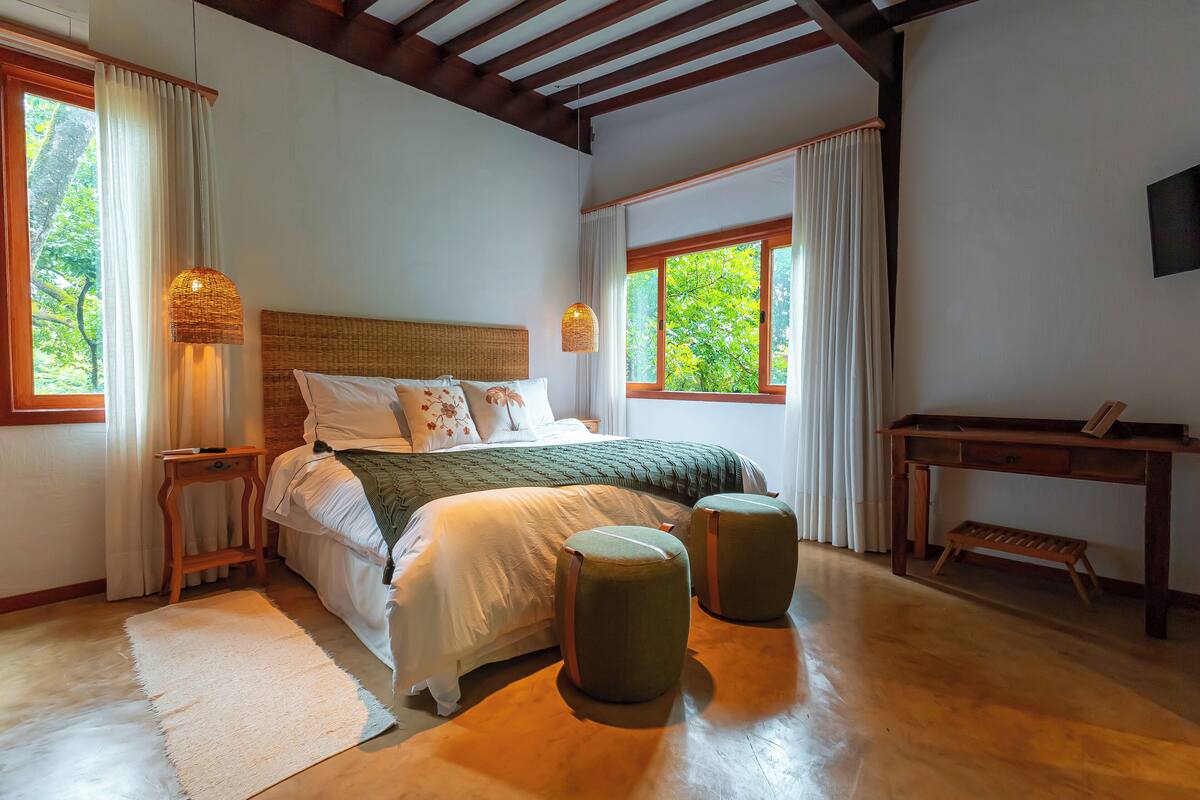 A bedroom with a bed, bedside tables, a wooden desk, and a window with a view of trees.