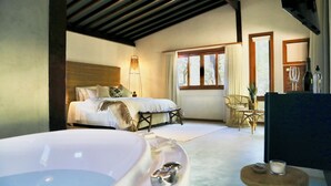 A bedroom with a large bathtub, a bed with pillows, a wicker chair, and a small table with a glass. - Boarã Lodge Natureza (Pirenópolis)