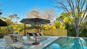 A swimming pool with lounge chairs and a table, surrounded by a wooden fence and trees. - Boarã Lodge Natureza (Pirenópolis)