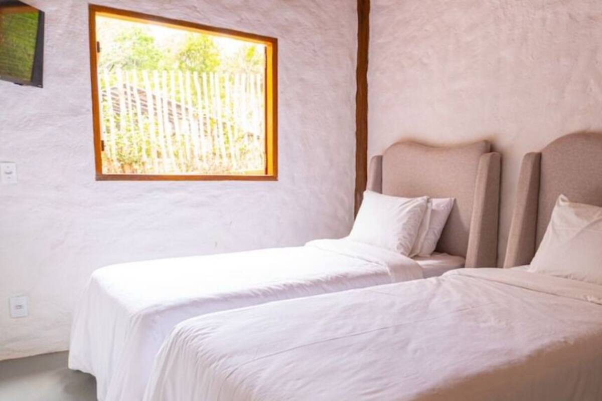 A room with two beds, a window with a view of a fence, and a textured wall.