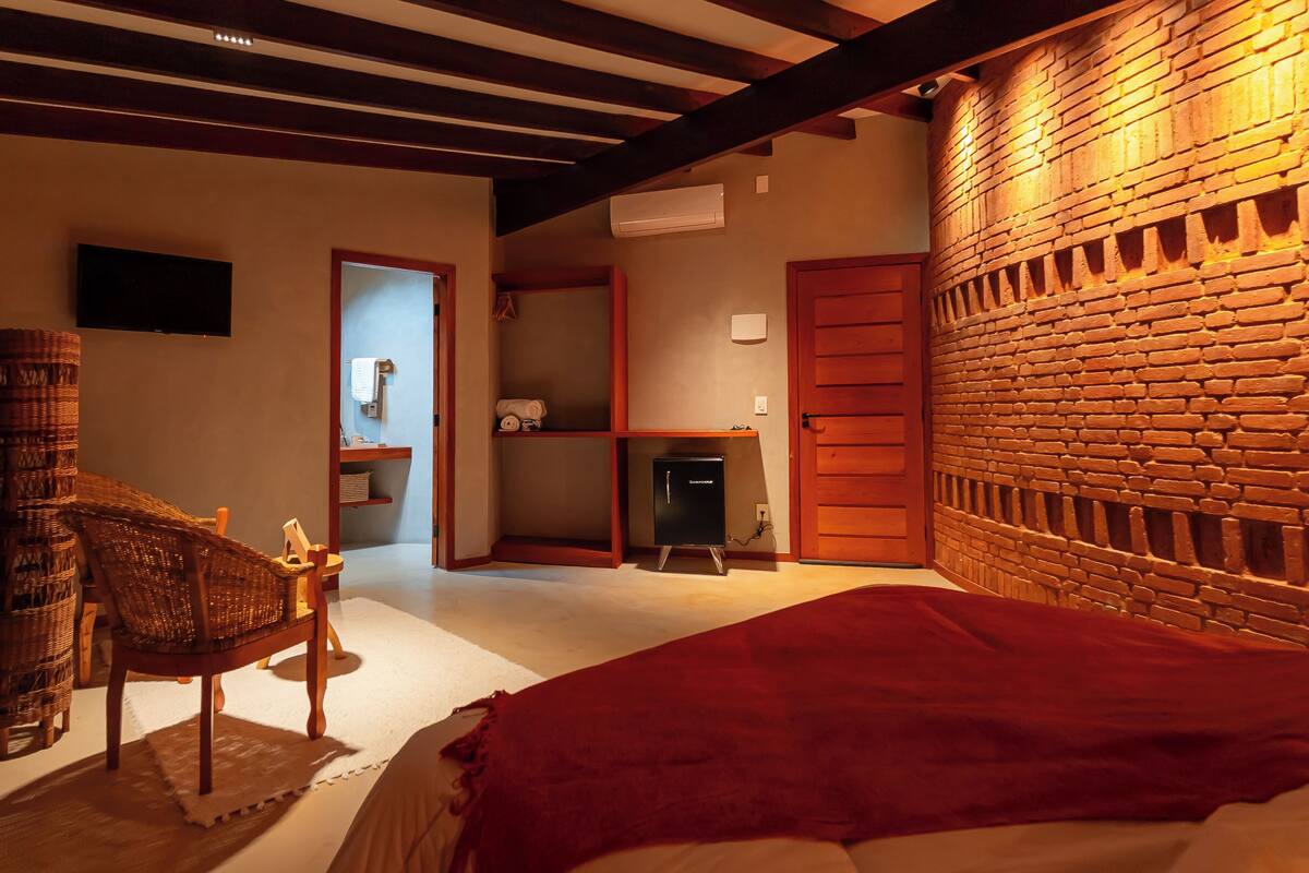 A room with a bed, a wooden bench, a television, a fireplace, and a brick wall.