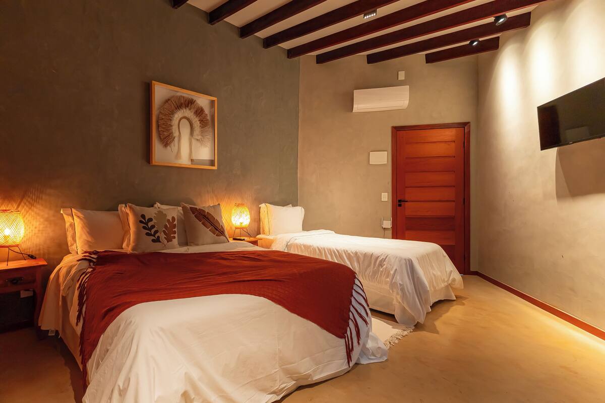 A bedroom with two beds, a wooden ceiling, a mounted TV, and a framed artwork on the wall.