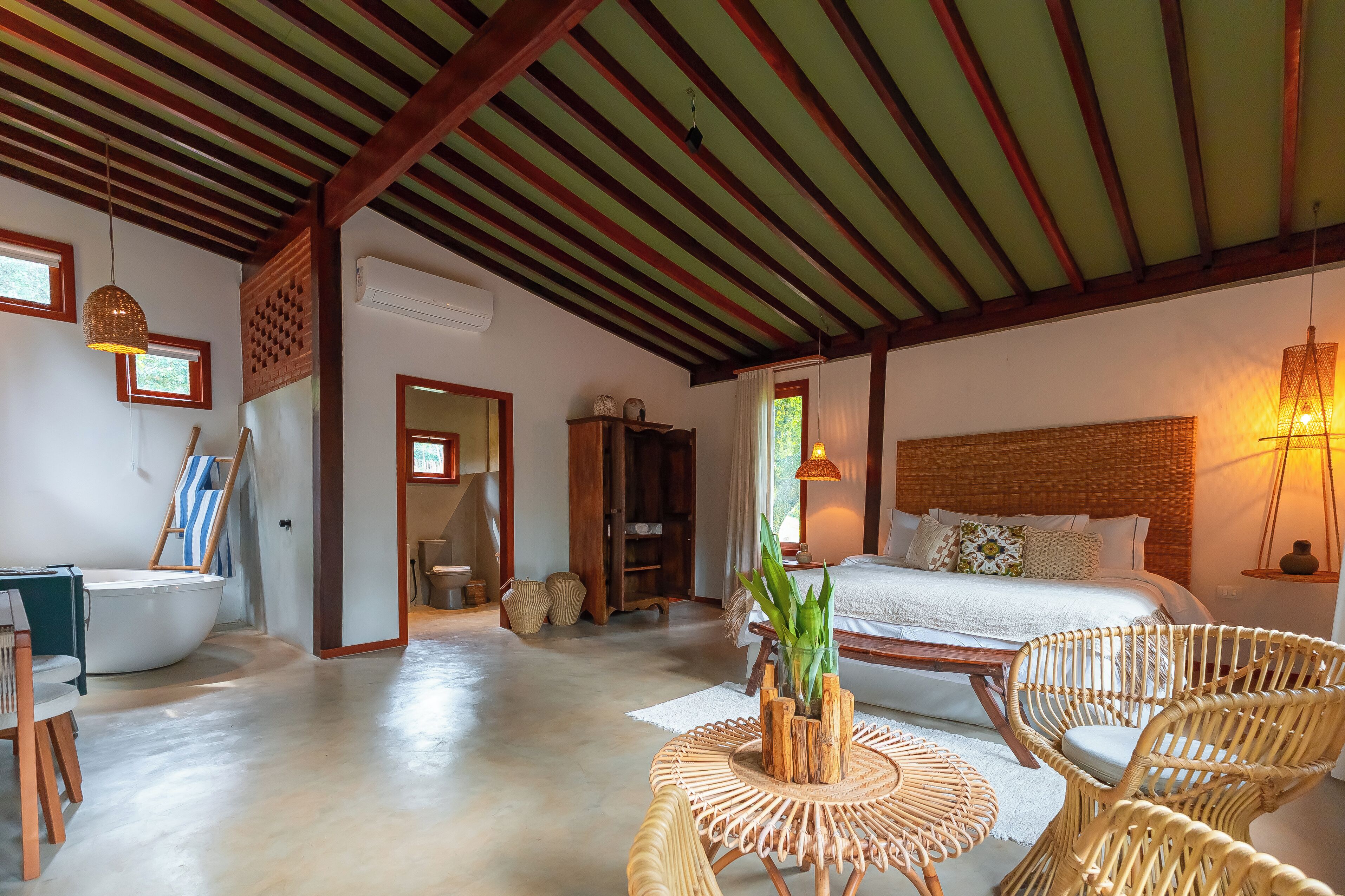 Um quarto espaçoso com uma cama grande, móveis de vime, uma mesinha e um barco.