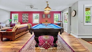 A pool table in a room with a red wall, wooden floor, and a ceiling fan.