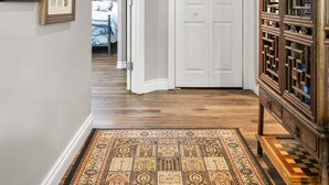 A hallway with patterned carpet, a wooden cabinet with glass doors, and a white door leading to a bedroom.