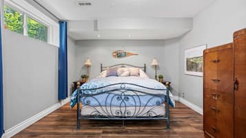 Een slaapkamer met een metalen bedframe, een houten dressoir en een raam met blauwe gordijnen.
