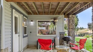 A covered patio with a stone pillar, a grill, and two red folding chairs.