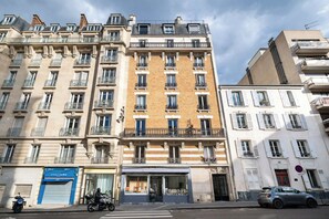 Un edificio de varios pisos con balcones, escaparates y coches aparcados.