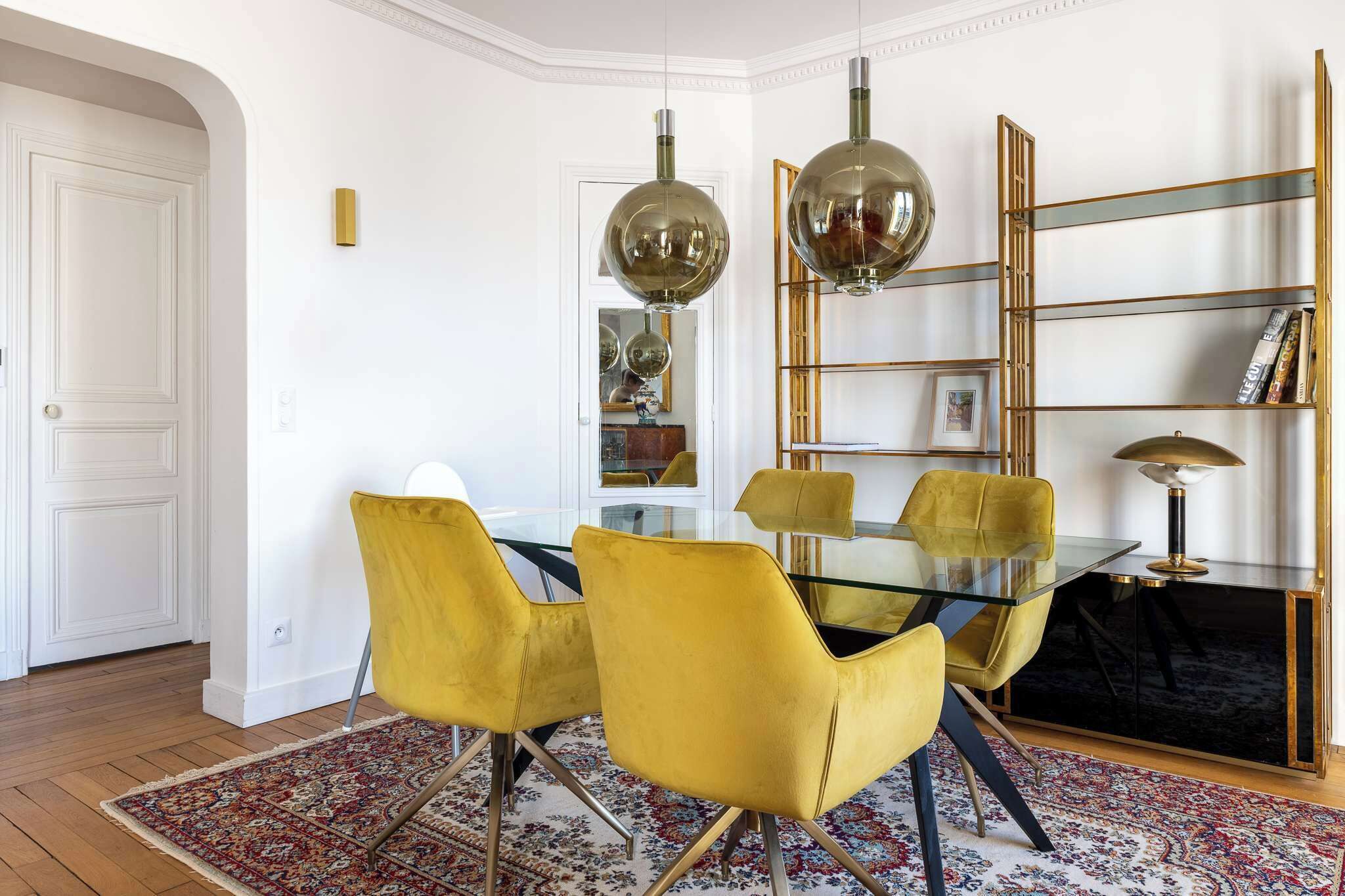 Een eethoek met een glazen tafel, gele stoelen en een zwarte console met een lamp.