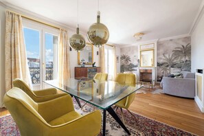 Uma sala de jantar com uma mesa de vidro, cadeiras amarelas e vista para a cidade através de amplas janelas.